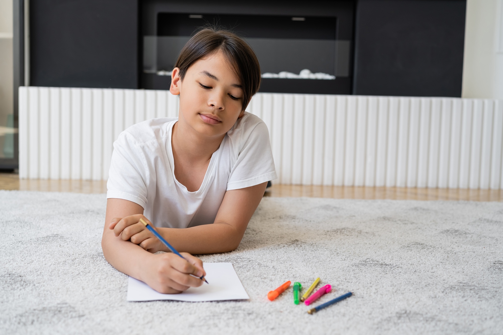 Asian boy with color pencil drawing on paper on floor at home