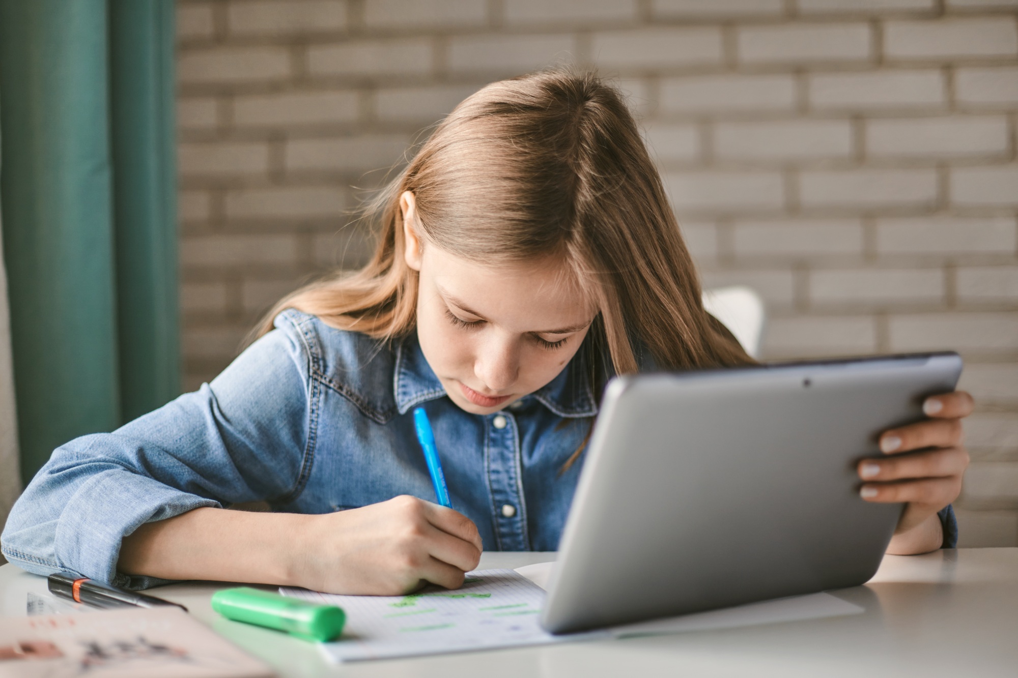 Cute teen schoolgirl does her homework with a tablet at home.
