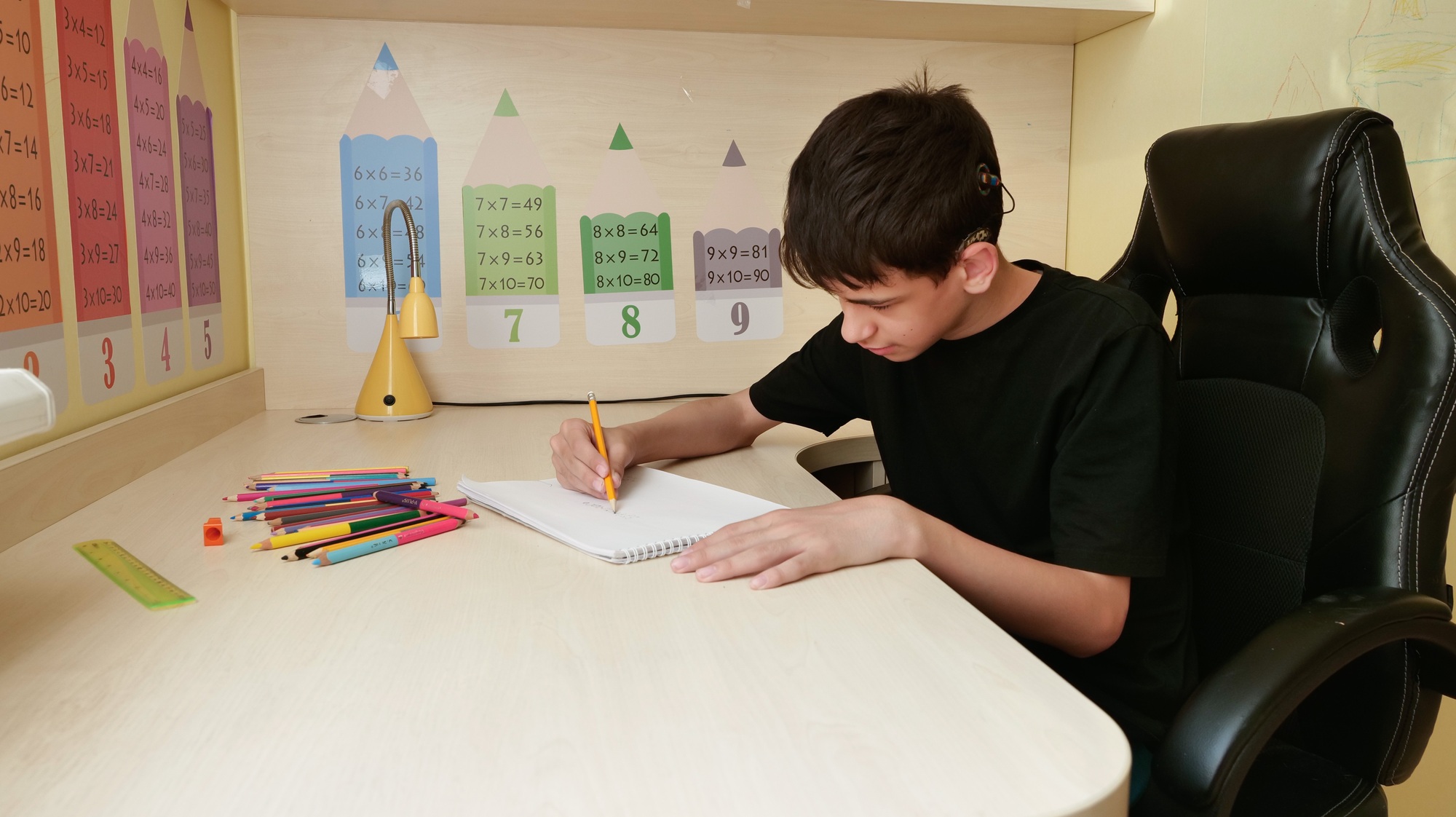 deaf teenager with cochlear implants draws with colored pencils at a desk