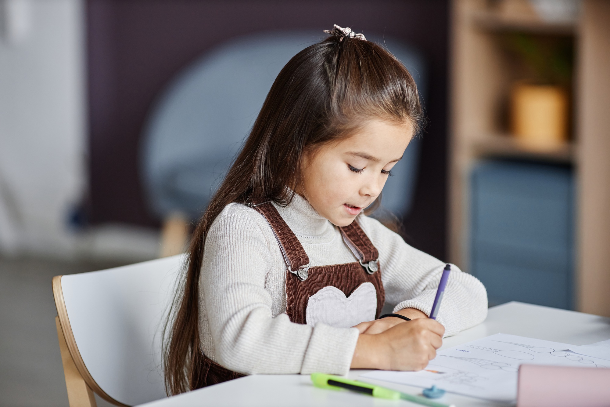 Diligent little girl with dark long hair drawing with crayons