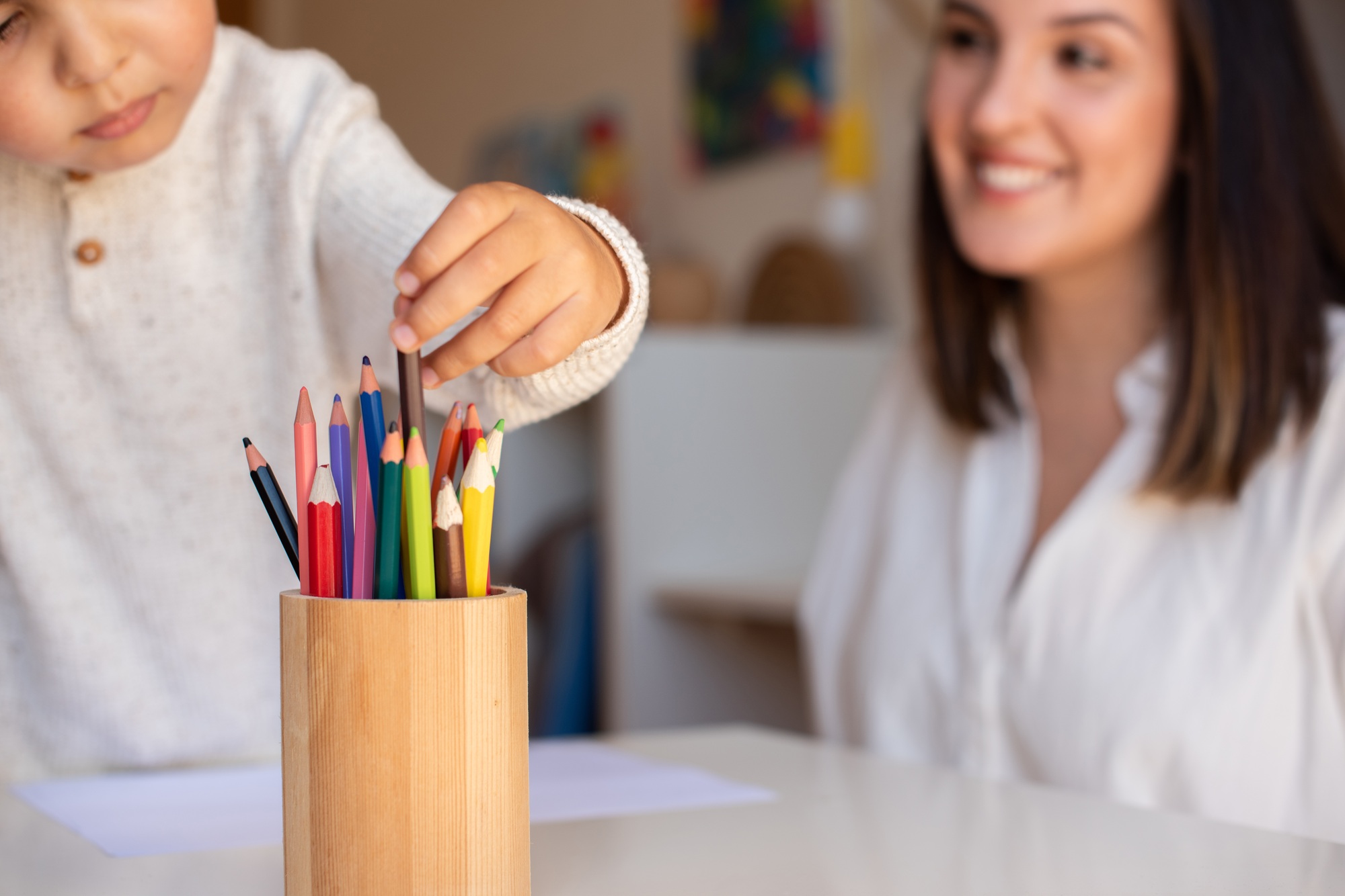 kid drawing with coloured pencils with mother or teacher educator. Focus on the pencils.
