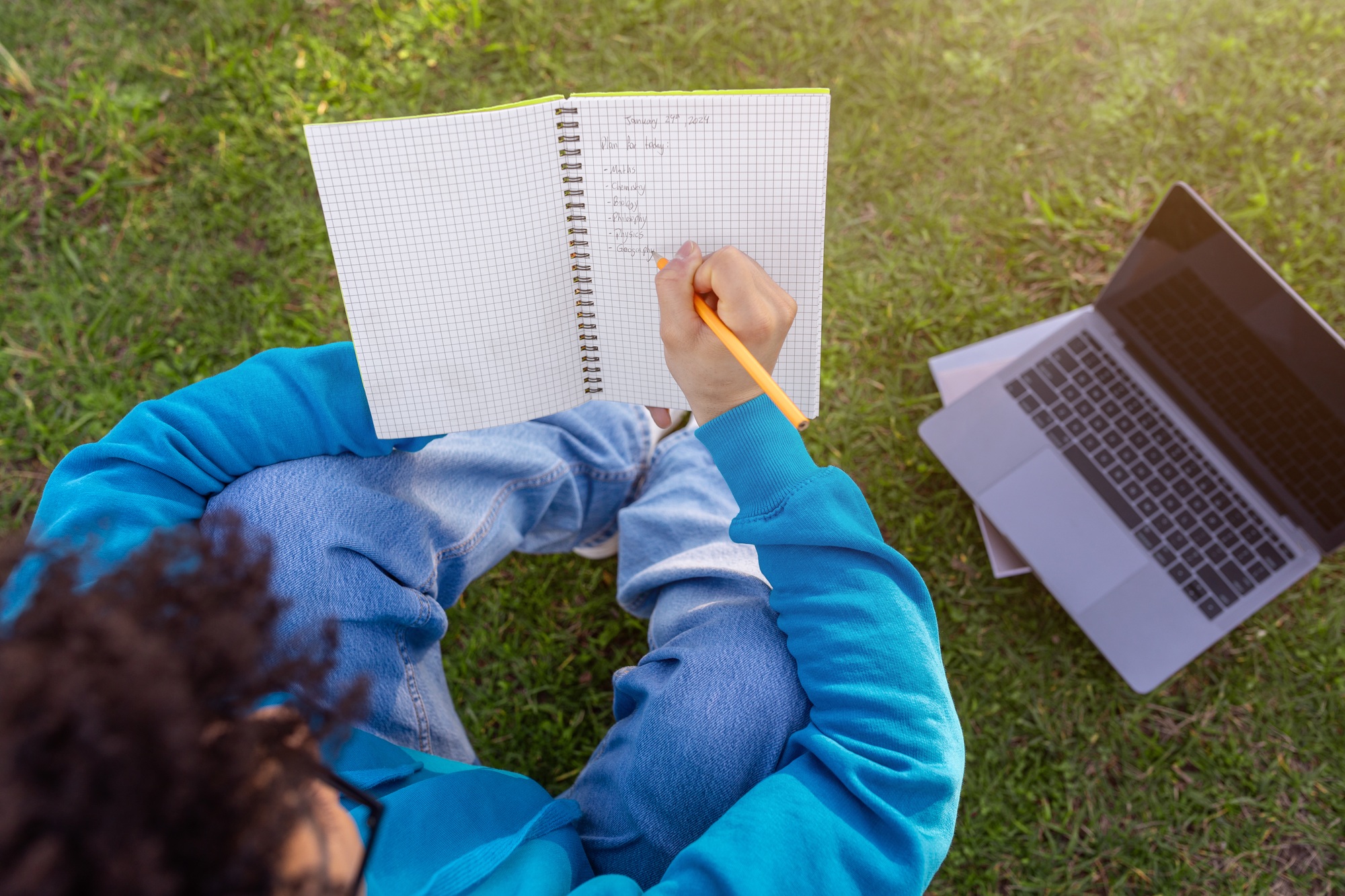 Rear view of student guy writing academic schedule sitting outdoors