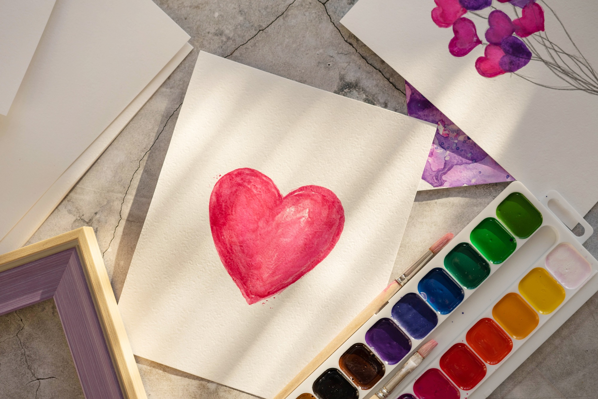 Watercolor drawing heart, palette, brushes in the sun.