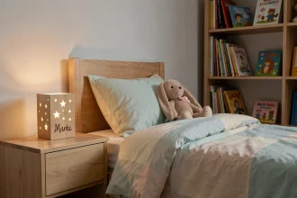 Veilleuse personnalisée en bois gravée avec le prénom d'un enfant posée sur une table de chevet dans une chambre cosy aux tons pastels